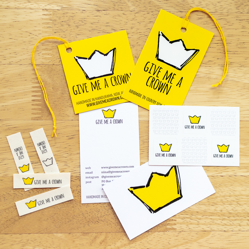 Product swing tags, a sticker sheet, business cards, and fabric labels on a wooden table.